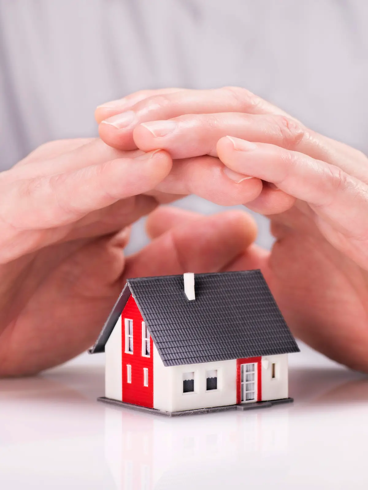 Hände legen sich schützend um ein Haus