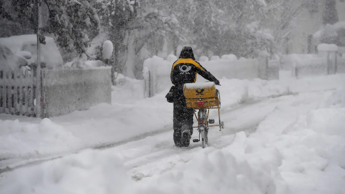 14.01.2021, Bayern, Garmisch-Partenkirchen: Ein Postbote schiebt sein Postfahrrad durch den Schnee. Innerhalb weniger Stunden sorgte eine Nordstaulage für viel frischen Schnee in den Bergen. Foto: Angelika Warmuth/dpa +++ dpa-Bildfunk +++