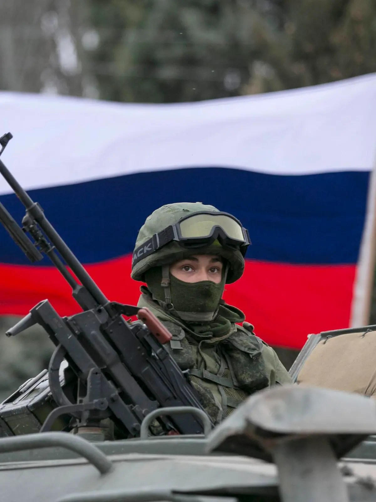 A pro-Russian man (not seen) holds a Russian flag behind an armed servicemen on top of a Russian army vehicle outside a Ukrainian border guard post in the Crimean town of Balaclava March 1, 2014. Ukraine accused Russia on Saturday of sending thousands of extra troops to Crimea and placed its military in the area on high alert as the Black Sea peninsula appeared to slip beyond Kiev's control. REUTERS/Baz Ratner (UKRAINE - Tags: MILITARY POLITICS CIVIL UNREST)