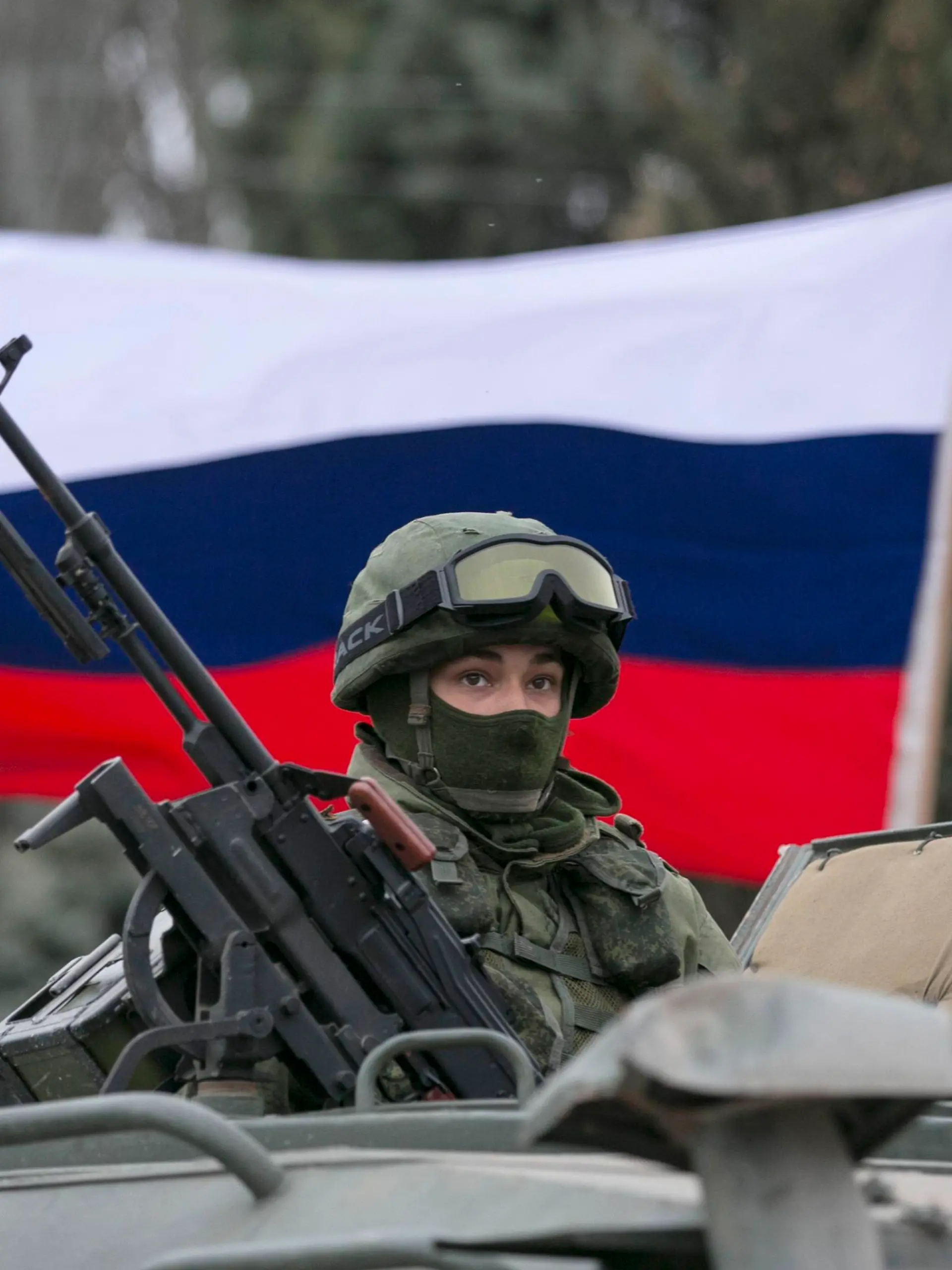 A pro-Russian man (not seen) holds a Russian flag behind an armed servicemen on top of a Russian army vehicle outside a Ukrainian border guard post in the Crimean town of Balaclava March 1, 2014. Ukraine accused Russia on Saturday of sending thousands of extra troops to Crimea and placed its military in the area on high alert as the Black Sea peninsula appeared to slip beyond Kiev's control. REUTERS/Baz Ratner (UKRAINE - Tags: MILITARY POLITICS CIVIL UNREST)