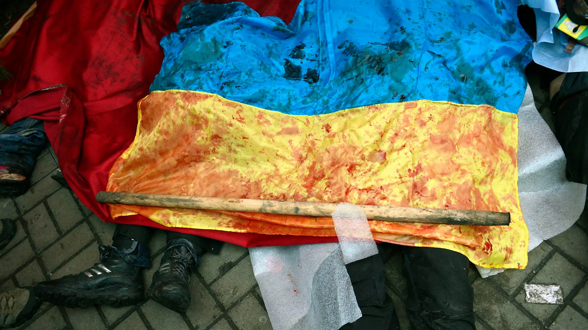 epa04090925 A bloody Ukranian flag covers the bodies of killed protesters in Kiev, Ukraine, 20 February 2014. More than 60 people have been killed in street fighting in Kiev on Thursday, the nationalist Svoboda opposition party says. The Ukrainian police force has been given combat weapons for use in the civil unrest in Kiev, Interior Minister Vitaliy Zakharchenko says. Fresh fighting broke out between thousands of protesters and riot police on Kiev's Independence Square only hours after opposition leaders and President Viktor Yanukovych declared a truce. Protesters were seen throwing firebombs and molotov cocktails at police, who responded with teargas. The square was filled with black smoke from burning tyres. EPA/LASZLO BELICZAY ATTENTION EDITORS: GRAPHIC CONTENT +++(c) dpa - Bildfunk+++
