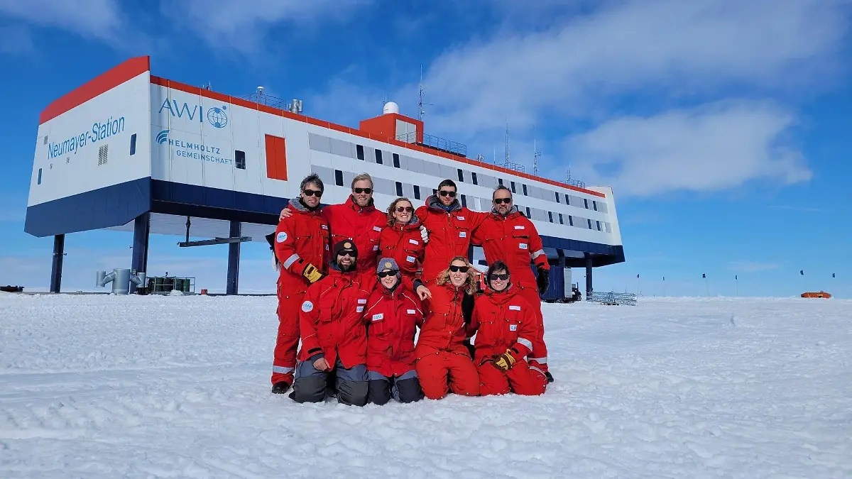 HANDOUT - 20.12.2022, Antarktis, Neumayer-Station: Das neunköpfige Überwinterungsteam posiert vor der Forschungsstation Neumayer III in der Antarktis. (zu dpa: «Antarktische Weihnachten mit Geschenken aus der Heimat») Foto: Markus Baden/AWI/dpa - ACHTUNG: Nur zur redaktionellen Verwendung im Zusammenhang mit der Berichterstattung über die Neumeyer III-Station und nur mit Urhebernennung Foto: AWI/Markus Baden +++ dpa-Bildfunk +++