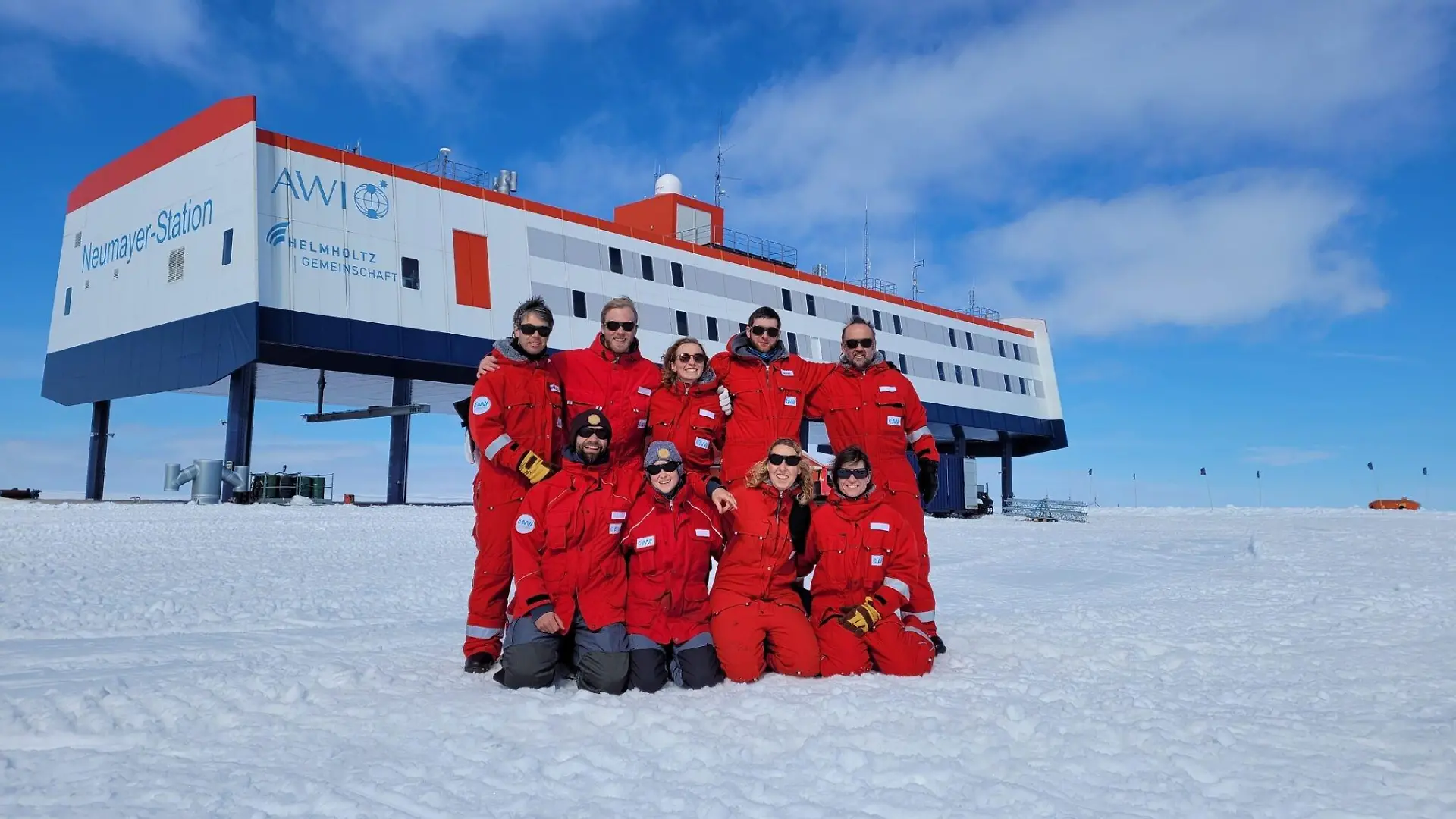 HANDOUT - 20.12.2022, Antarktis, Neumayer-Station: Das neunköpfige Überwinterungsteam posiert vor der Forschungsstation Neumayer III in der Antarktis. (zu dpa: «Antarktische Weihnachten mit Geschenken aus der Heimat») Foto: Markus Baden/AWI/dpa - ACHTUNG: Nur zur redaktionellen Verwendung im Zusammenhang mit der Berichterstattung über die Neumeyer III-Station und nur mit Urhebernennung Foto: AWI/Markus Baden +++ dpa-Bildfunk +++