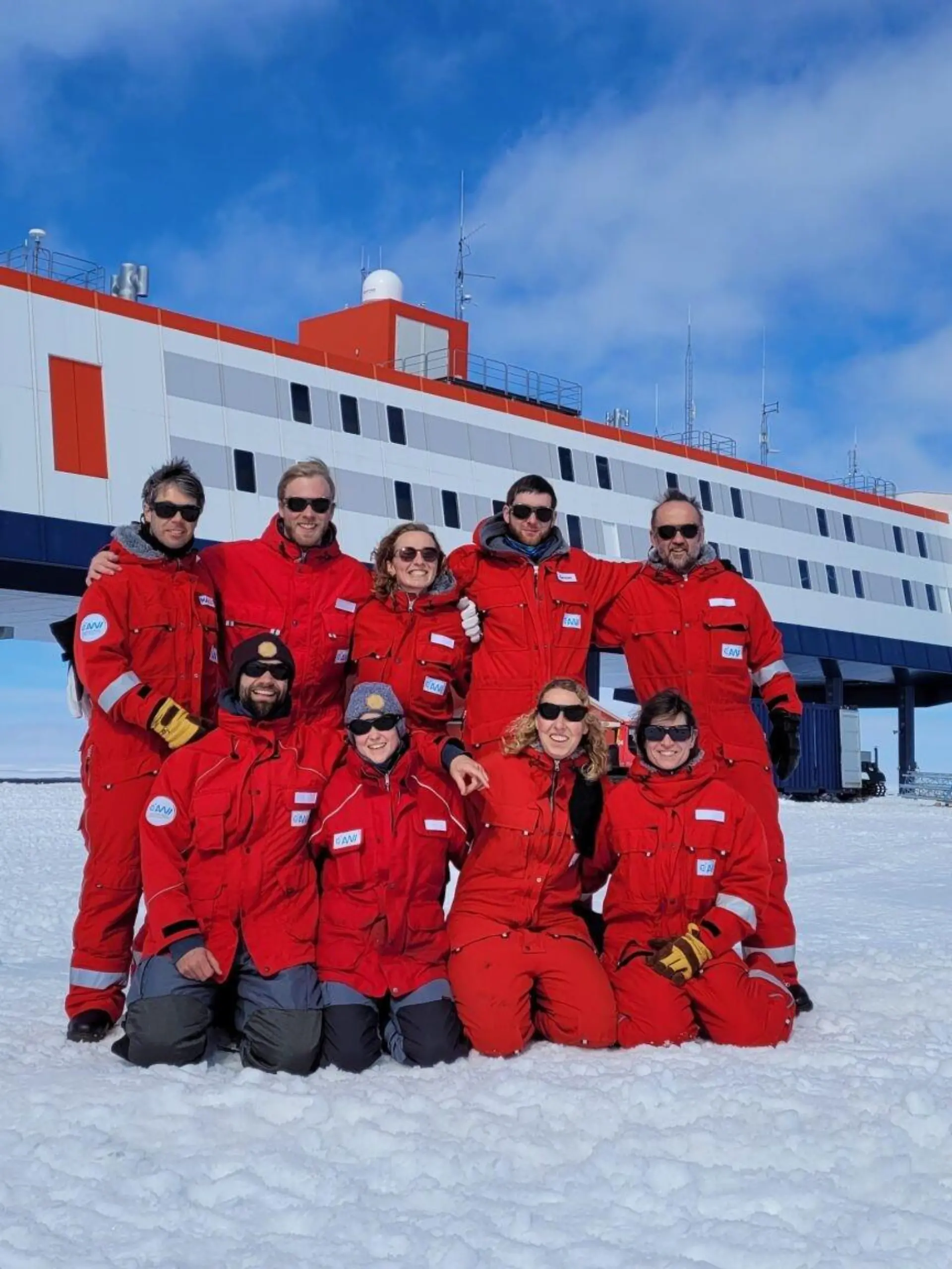 HANDOUT - 20.12.2022, Antarktis, Neumayer-Station: Das neunköpfige Überwinterungsteam posiert vor der Forschungsstation Neumayer III in der Antarktis. (zu dpa: «Antarktische Weihnachten mit Geschenken aus der Heimat») Foto: Markus Baden/AWI/dpa - ACHTUNG: Nur zur redaktionellen Verwendung im Zusammenhang mit der Berichterstattung über die Neumeyer III-Station und nur mit Urhebernennung Foto: AWI/Markus Baden +++ dpa-Bildfunk +++