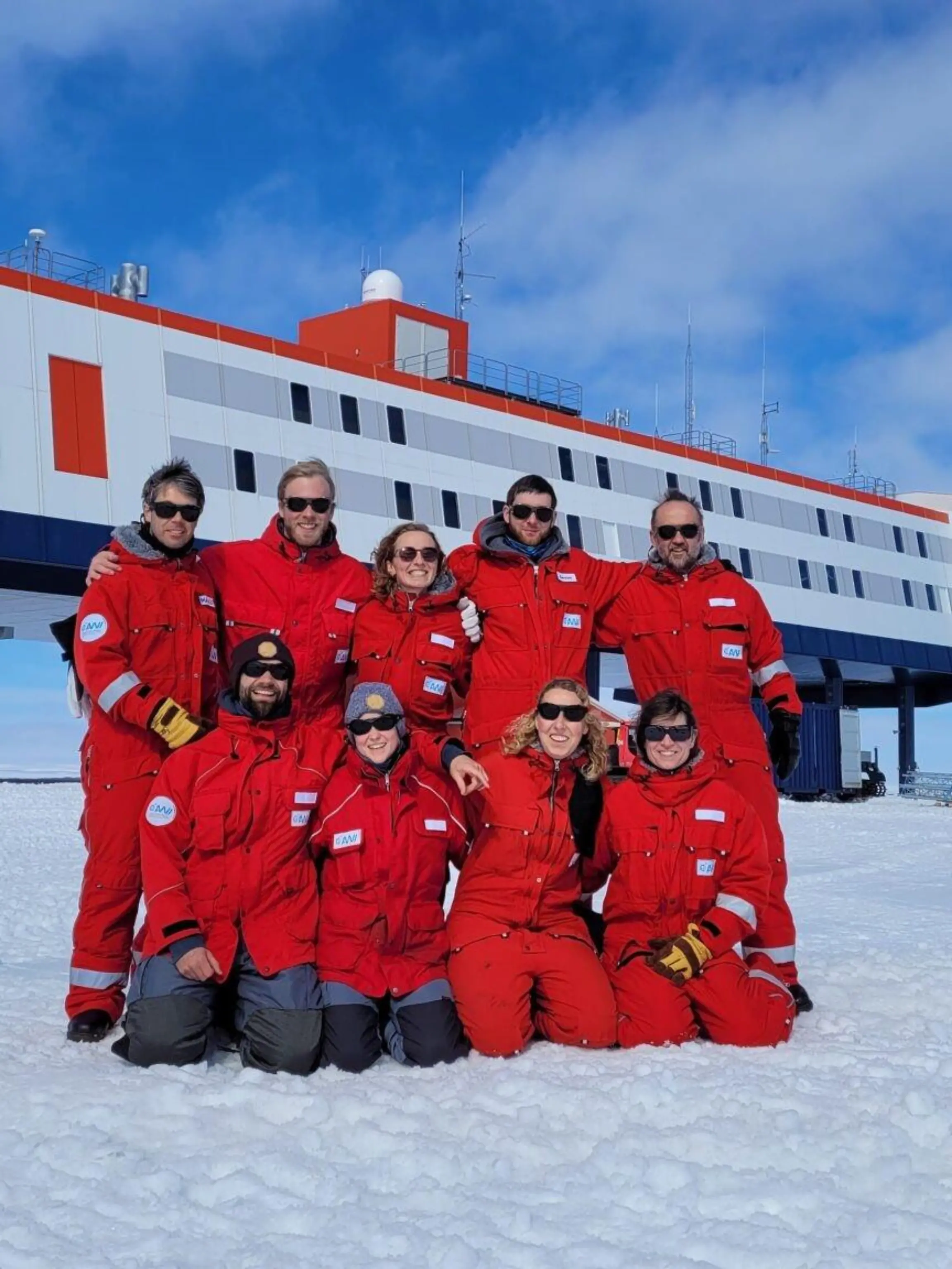 HANDOUT - 20.12.2022, Antarktis, Neumayer-Station: Das neunköpfige Überwinterungsteam posiert vor der Forschungsstation Neumayer III in der Antarktis. (zu dpa: «Antarktische Weihnachten mit Geschenken aus der Heimat») Foto: Markus Baden/AWI/dpa - ACHTUNG: Nur zur redaktionellen Verwendung im Zusammenhang mit der Berichterstattung über die Neumeyer III-Station und nur mit Urhebernennung Foto: AWI/Markus Baden +++ dpa-Bildfunk +++