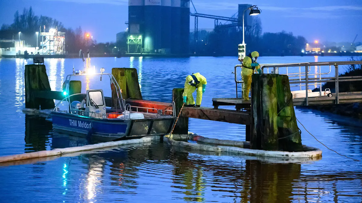 21.12.2022, Schleswig-Holstein, Brunsbüttel: Einsatzkräfte des THW in Schutzanzügen arbeiten mit Ölschlengeln an einem Steg. Aus einem Leck in einer Pipeline im Hafen von Brunsbüttel sind große Mengen Öl in den Nord-Ostsee-Kanal gelaufen. Foto: Jonas Walzberg/dpa +++ dpa-Bildfunk +++