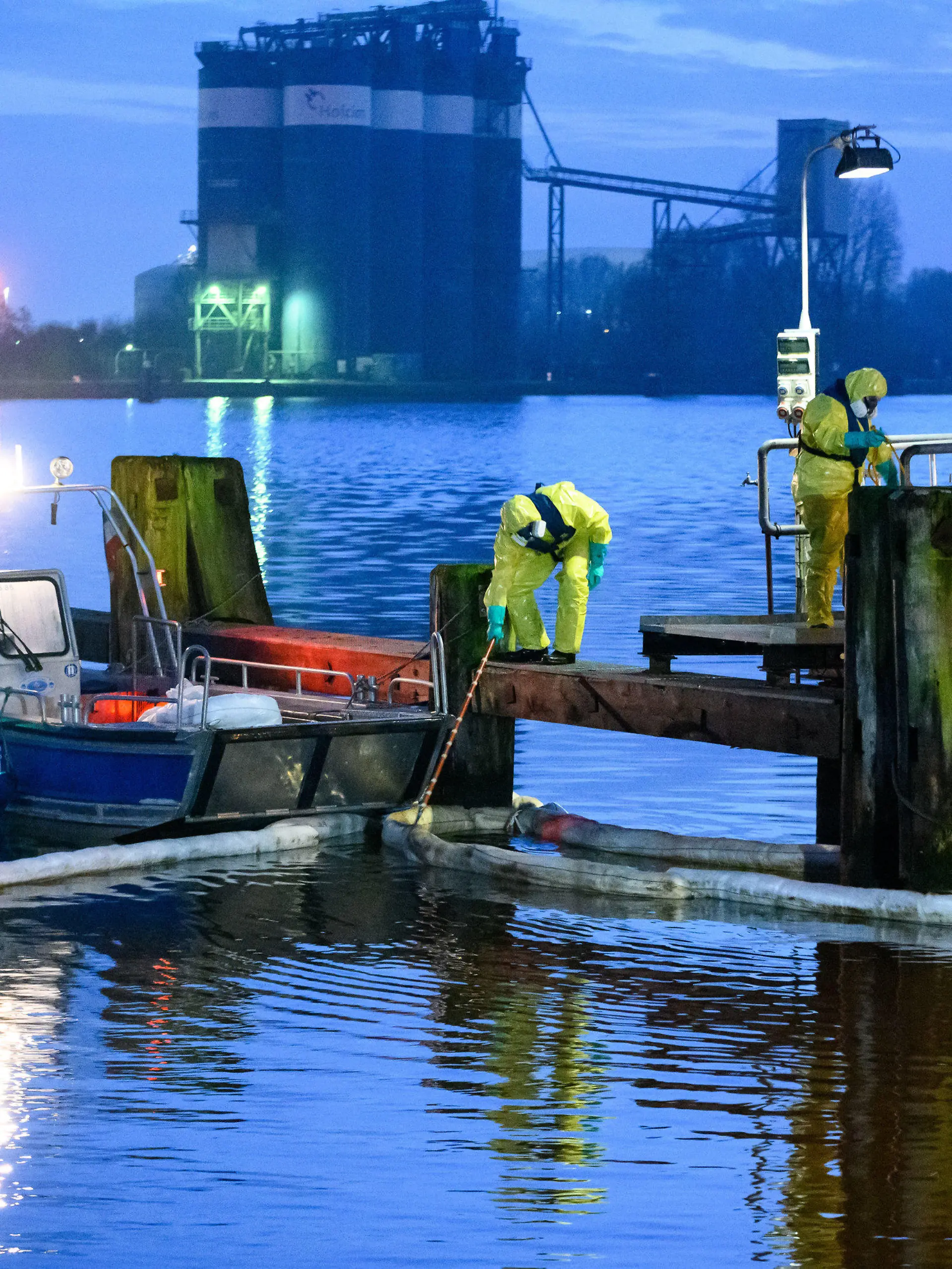 21.12.2022, Schleswig-Holstein, Brunsbüttel: Einsatzkräfte des THW in Schutzanzügen arbeiten mit Ölschlengeln an einem Steg. Aus einem Leck in einer Pipeline im Hafen von Brunsbüttel sind große Mengen Öl in den Nord-Ostsee-Kanal gelaufen. Foto: Jonas Walzberg/dpa +++ dpa-Bildfunk +++