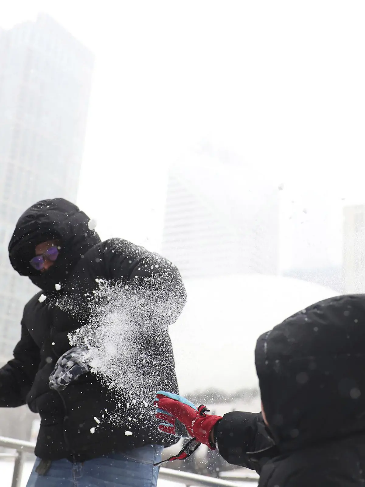 22.12.2022, USA, Chicago: Andres Garduno (l) liefert sich mit seinem Sohn Matteo Jimenez Garduno, beide aus Mexiko, während des Wintersturms am Donnerstag auf der Eisbahn im Millennium Park eine Schneeschlacht. In ganz Chicago fiel heute Schnee, und die Temperaturen sollen bis zum Abend drastisch sinken. Die USA bereiten sich auf einen «historischen» Wintersturm kurz vor den Weihnachtsfeiertagen vor. Eine arktische Kaltfront werde in der Nacht von Donnerstag auf Freitag (Ortszeit) über Teile im Osten Landes hinwegziehen, warnte der US-Wetterdienst. Das Sturmtief werde extreme Kälte, heftige Schneefälle und Eiswind bringen. Foto: Michael Blackshire/Chicago Tribune via ZUMA Press/dpa +++ dpa-Bildfunk +++