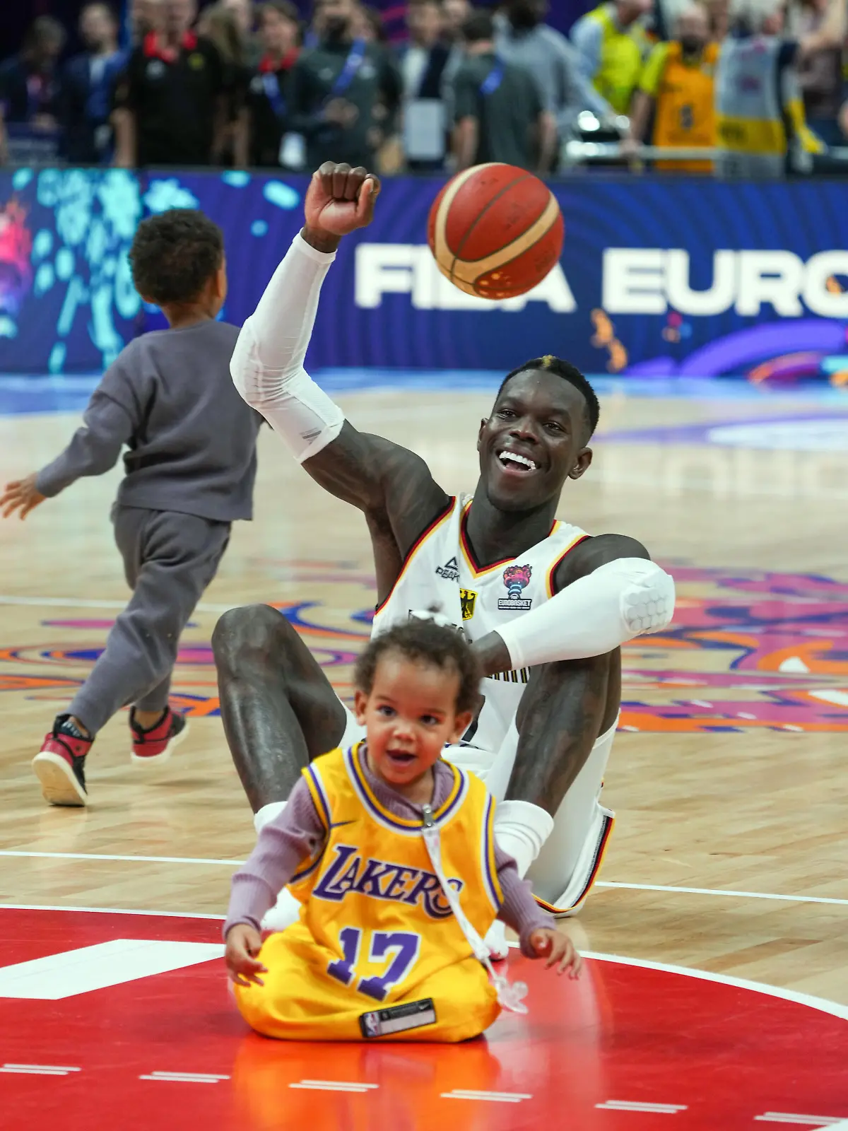 ARCHIV - 13.09.2022, Berlin: Basketball: EM, Deutschland - Griechenland, K.o.-Runde, Viertelfinale, Mercedes-Benz Arena, Dennis Schröder (Deutschland) sitzt nach dem Spiel mit seinen beiden Kindern auf dem Spielfeld. (zu dpa: «Schröder: Bescherung für Kinder wegen NBA-Auswärtsspiel vorziehen») Foto: Soeren Stache/dpa +++ dpa-Bildfunk +++