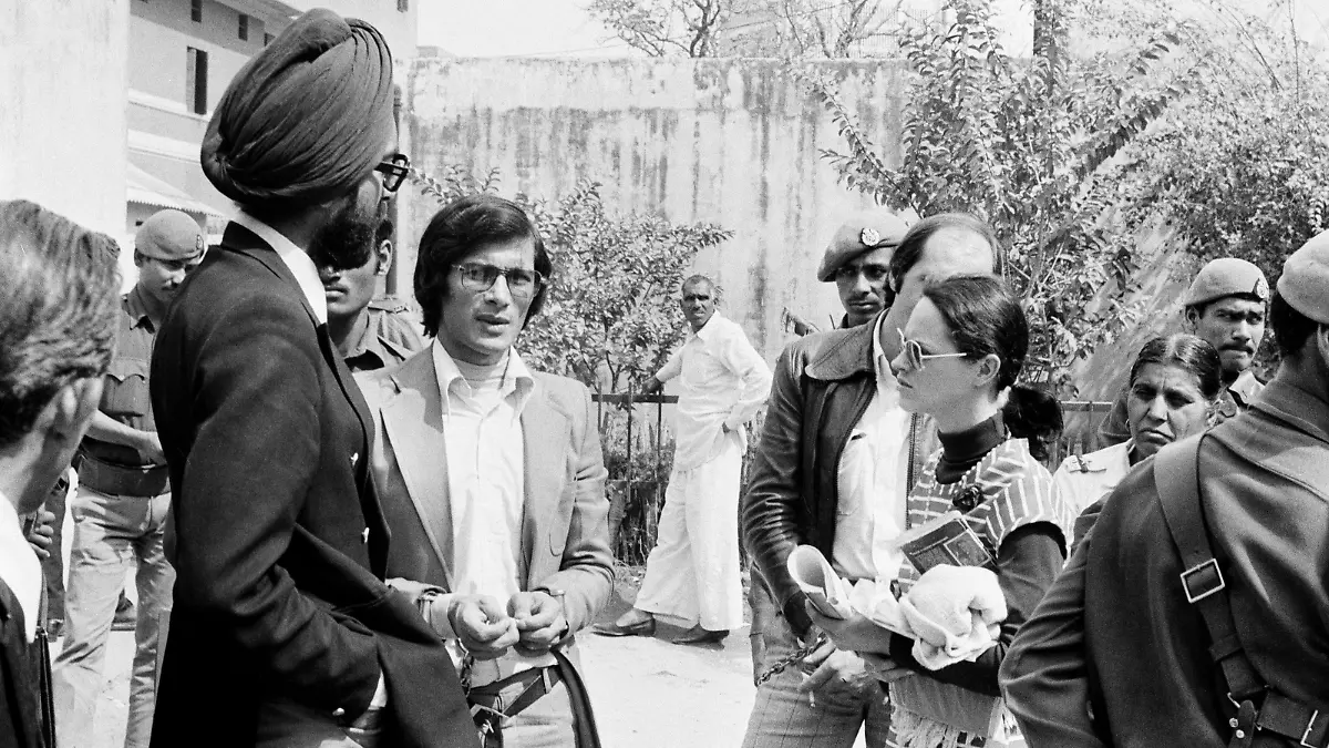 Charles Sobhraj, center, the alleged leader of an Asian murder ring, and his girlfriend Marie-Andree Leclerc, striped dress, wait outside of court during one of their appearances, in New Delhi, India, Feb. 24, 1977. They are in court for preliminary hearings into whether they should be charged with the drugging, robbing and murder of foreign tourists. They were arrested here last July and are also wanted by authorities in Thailand. (AP Photo)