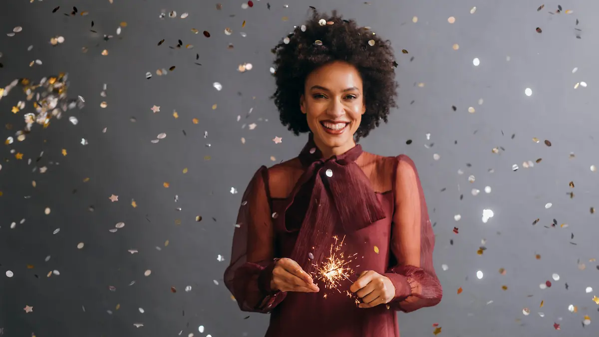 A portrait of a smiling Afro American woman holding a New Year's sprinkler (grey background)