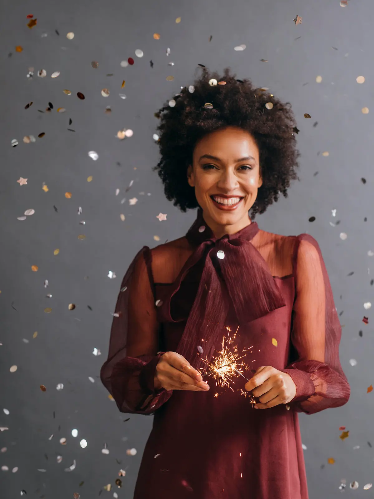 A portrait of a smiling Afro American woman holding a New Year's sprinkler (grey background)