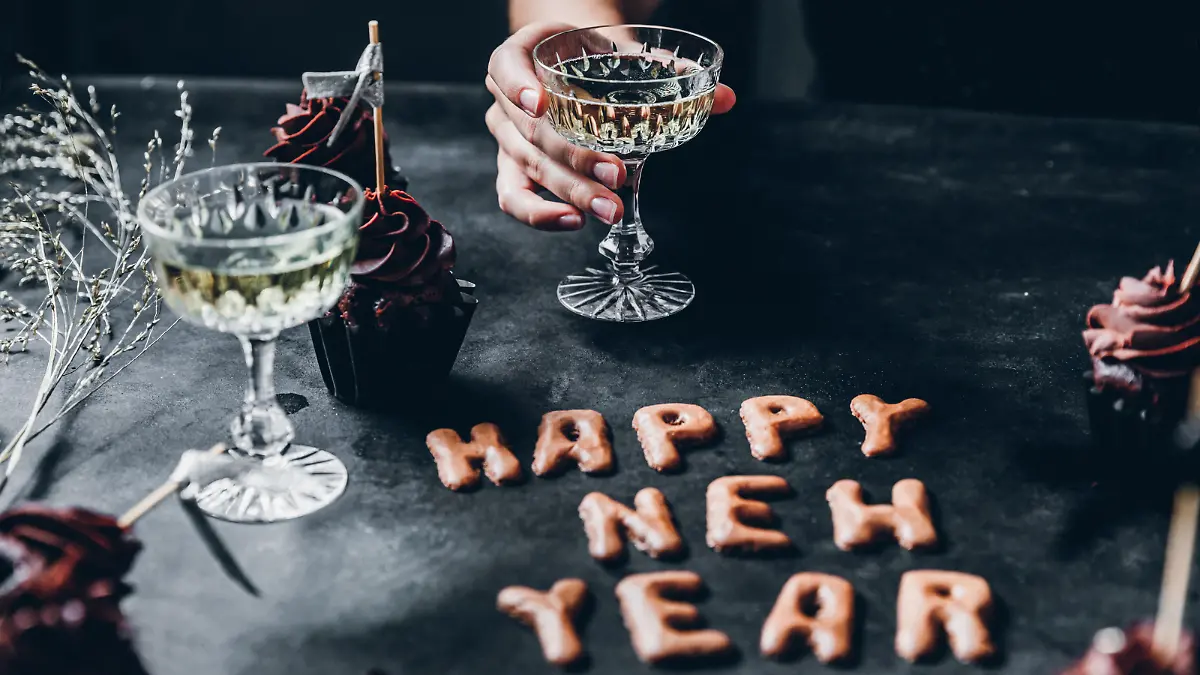 Happy new year cookie on table with cupcakes and a woman sitting holding a glass of champagne.