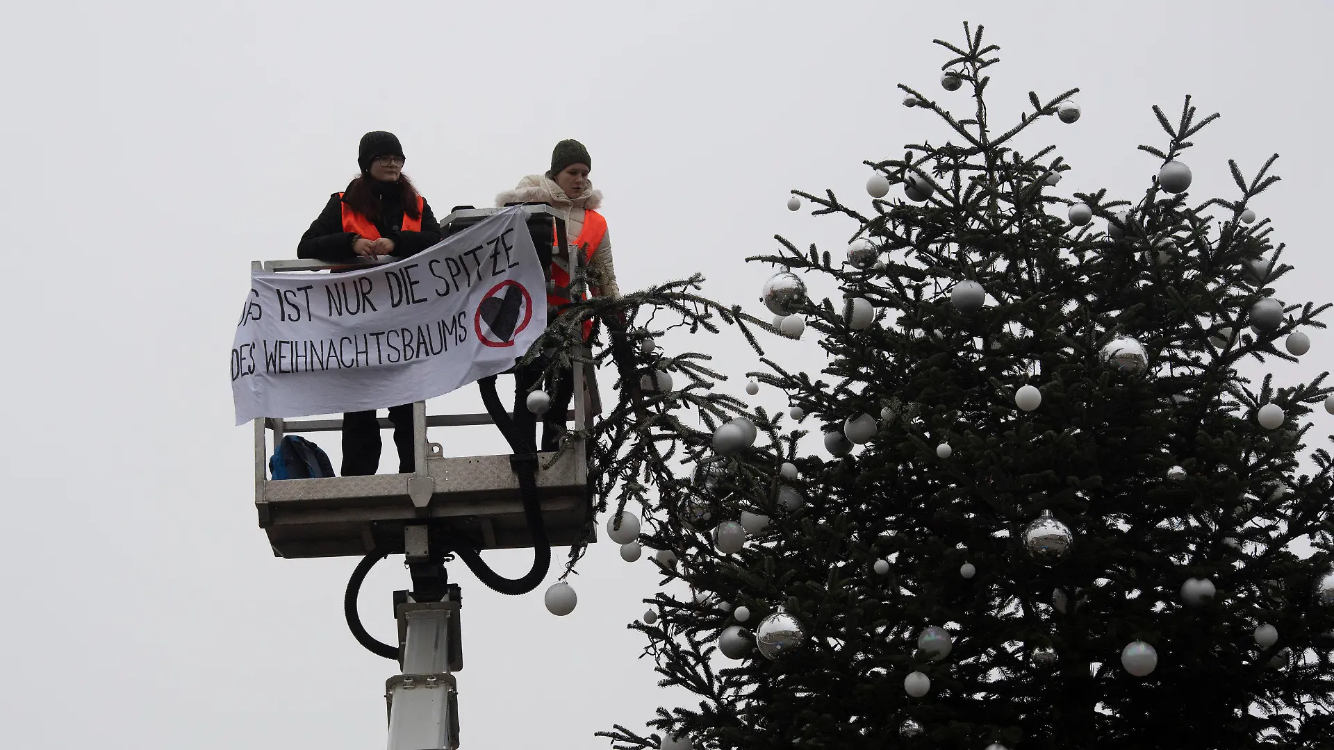 21.12.2022, Berlin: Ohne Spitze steht der Weihnachtsbaum vor dem Brandenburger Tor. Zwei Aktivisten der Umweltschutzgruppe Letzte Generation fuhren mit einem Hubwagen vor dem Tannenbaum auf dem Pariser Platz am Brandenburger Tor. Sie entrollten ein Transparent und entfernten dann die Spitze des Weihnachtsbaums. Foto: Paul Zinken/dpa +++ dpa-Bildfunk +++