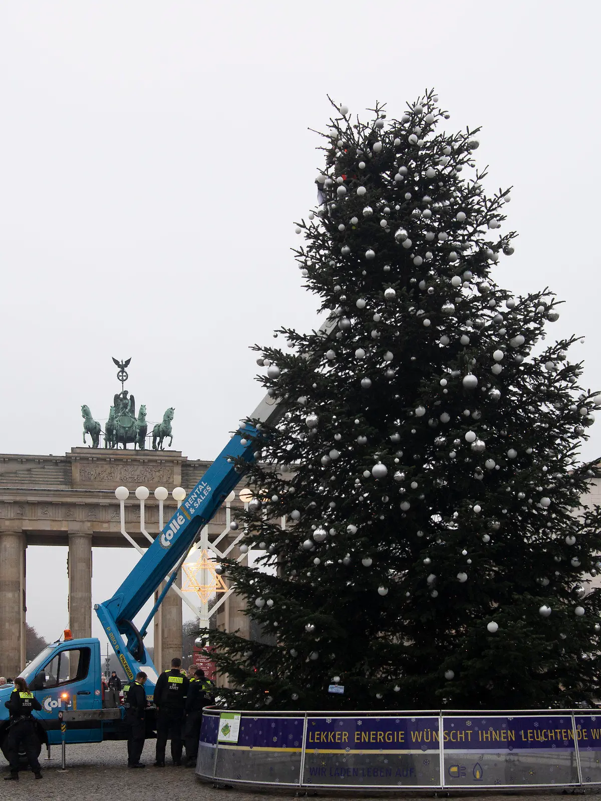 21.12.2022, Berlin: Ohne Spitze steht der Weihnachtsbaum vor dem Brandenburger Tor. Zwei Aktivisten der Umweltschutzgruppe Letzte Generation fuhren mit einem Hubwagen vor dem Tannenbaum auf dem Pariser Platz am Brandenburger Tor. Sie entrollten ein Transparent und entfernten dann die Spitze des Weihnachtsbaums. Foto: Paul Zinken/dpa +++ dpa-Bildfunk +++