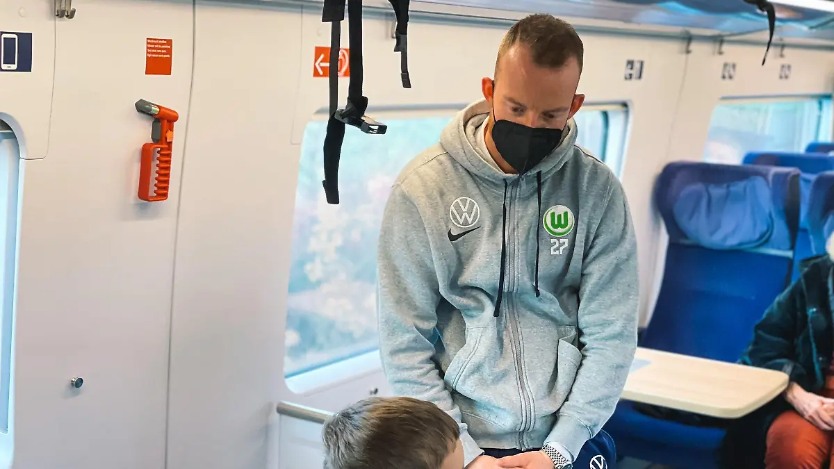 Die Maske sitzt: Wolfsburg-Kapitän Maximilian Arnold spricht im ICE mit einem Kind.