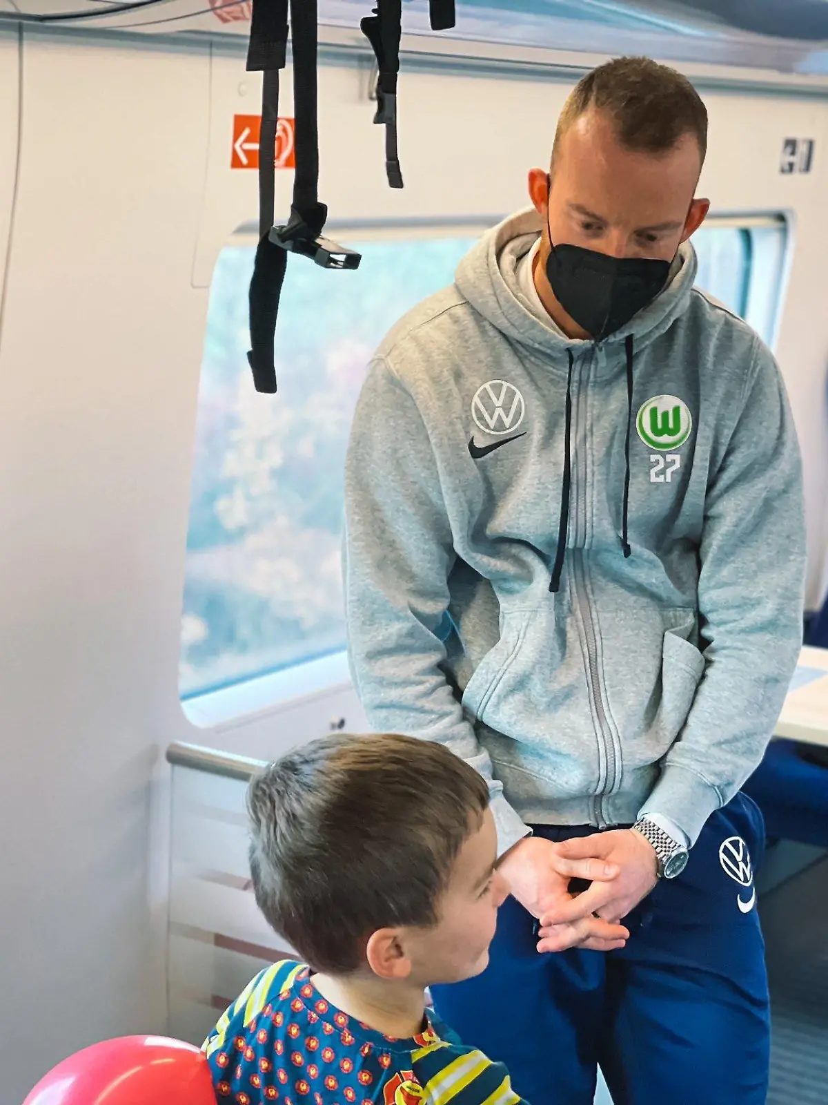 Die Maske sitzt: Wolfsburg-Kapitän Maximilian Arnold spricht im ICE mit einem Kind.