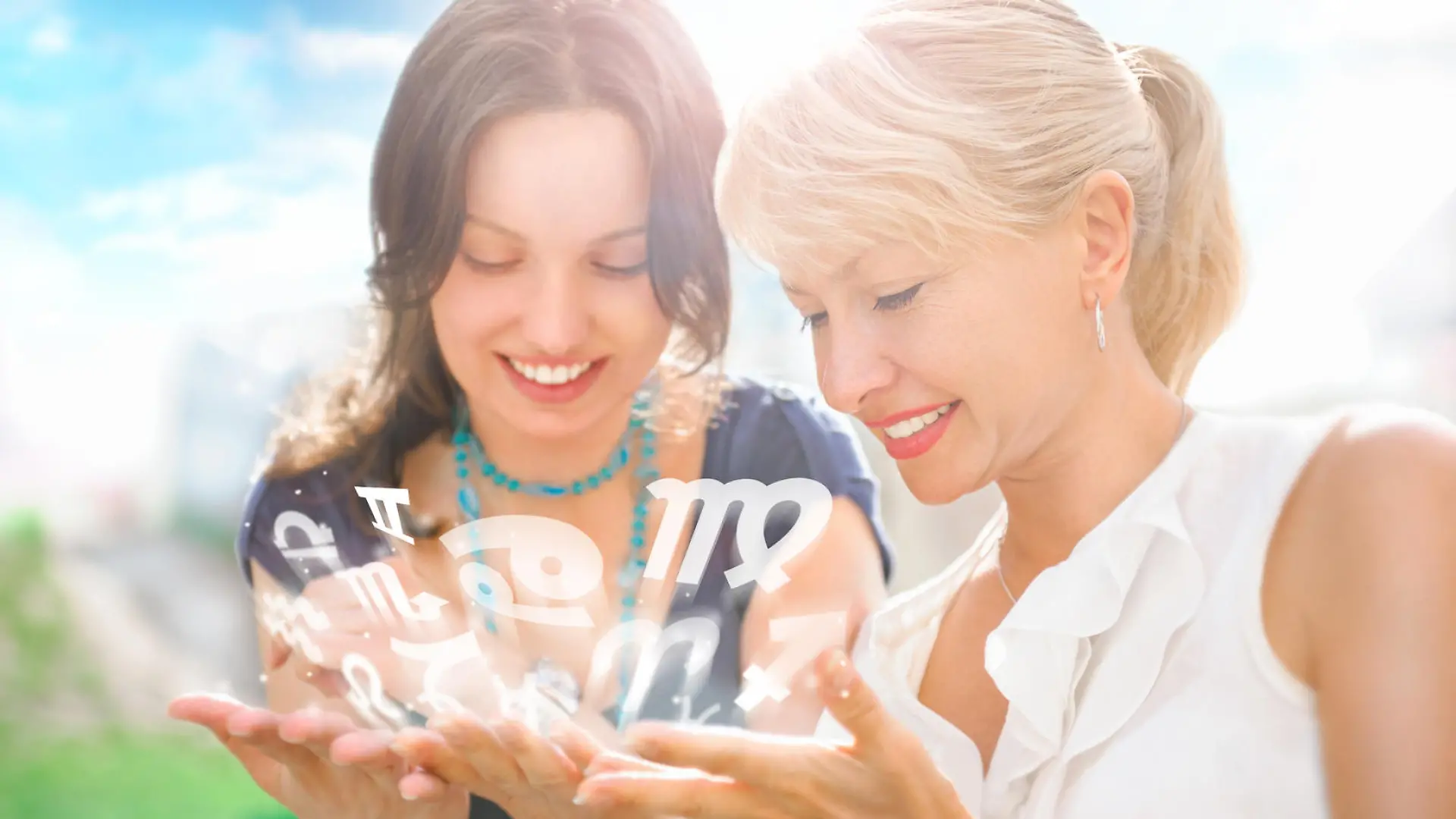 Two women mother and daughter sitting at summer park and having fun while discussing horoscope and different zodiac symbols appearing from their hands