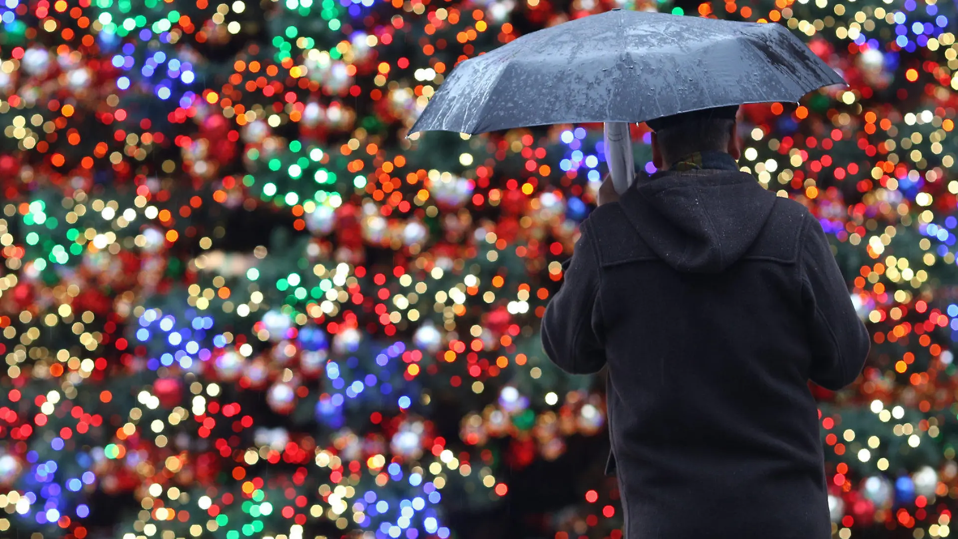 Ein Mann mit Regenschirm steht am 29.11.2012 auf dem Weihnachtsmarkt am Potsdamer Platz in Berlin vor einem beleuchteten Weihnachtsbaum. Das Wetter in der Hauptstadt zeigt sich weiterhin von seiner regnerischen Seite, die Weihnachtsmärkte hoffen aber auf Schnee, der für das Wochenende angekündigt wurde. Foto: Florian Schuh/dpa +++(c) dpa - Bildfunk+++