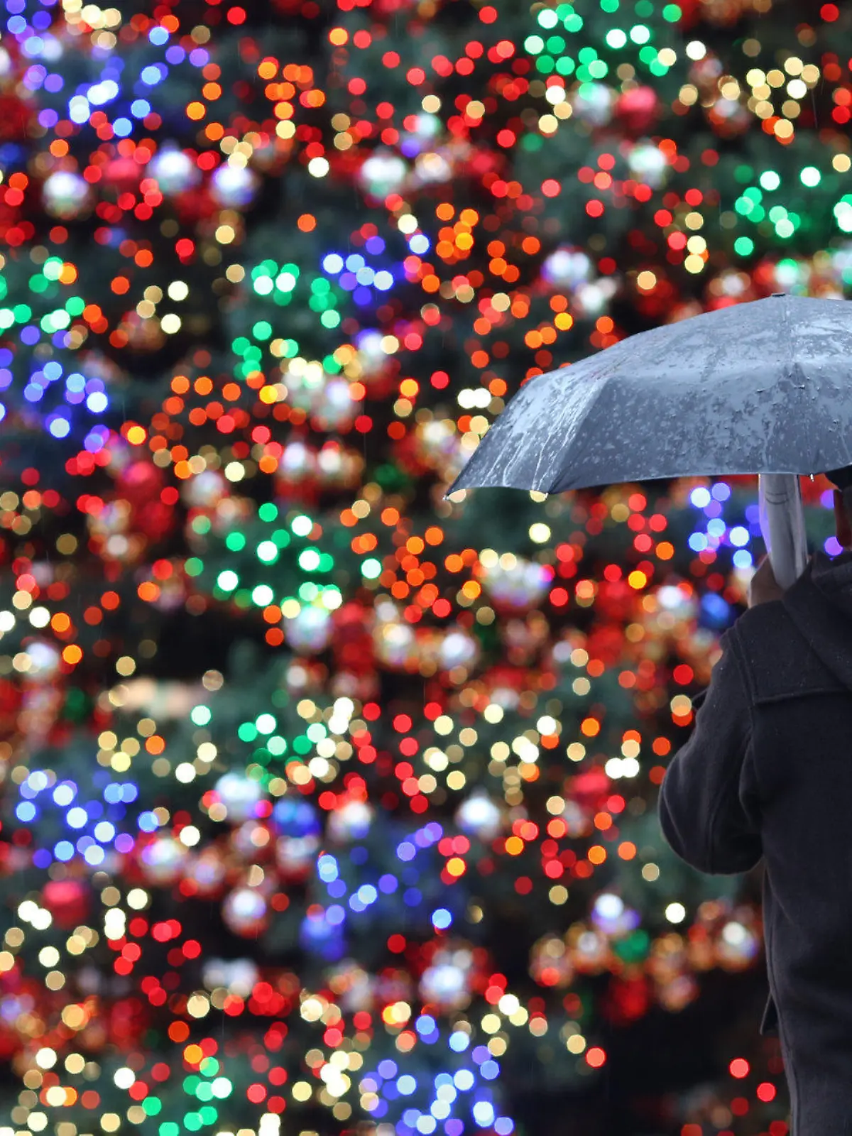 Ein Mann mit Regenschirm steht am 29.11.2012 auf dem Weihnachtsmarkt am Potsdamer Platz in Berlin vor einem beleuchteten Weihnachtsbaum. Das Wetter in der Hauptstadt zeigt sich weiterhin von seiner regnerischen Seite, die Weihnachtsmärkte hoffen aber auf Schnee, der für das Wochenende angekündigt wurde. Foto: Florian Schuh/dpa  +++(c) dpa - Bildfunk+++