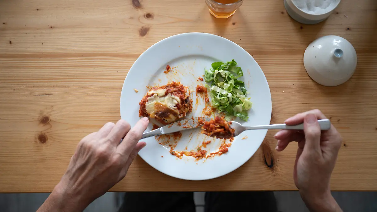 Ein Mann isst eine vegetarische Lasagne aus Linsen mit einem grünen Salat.