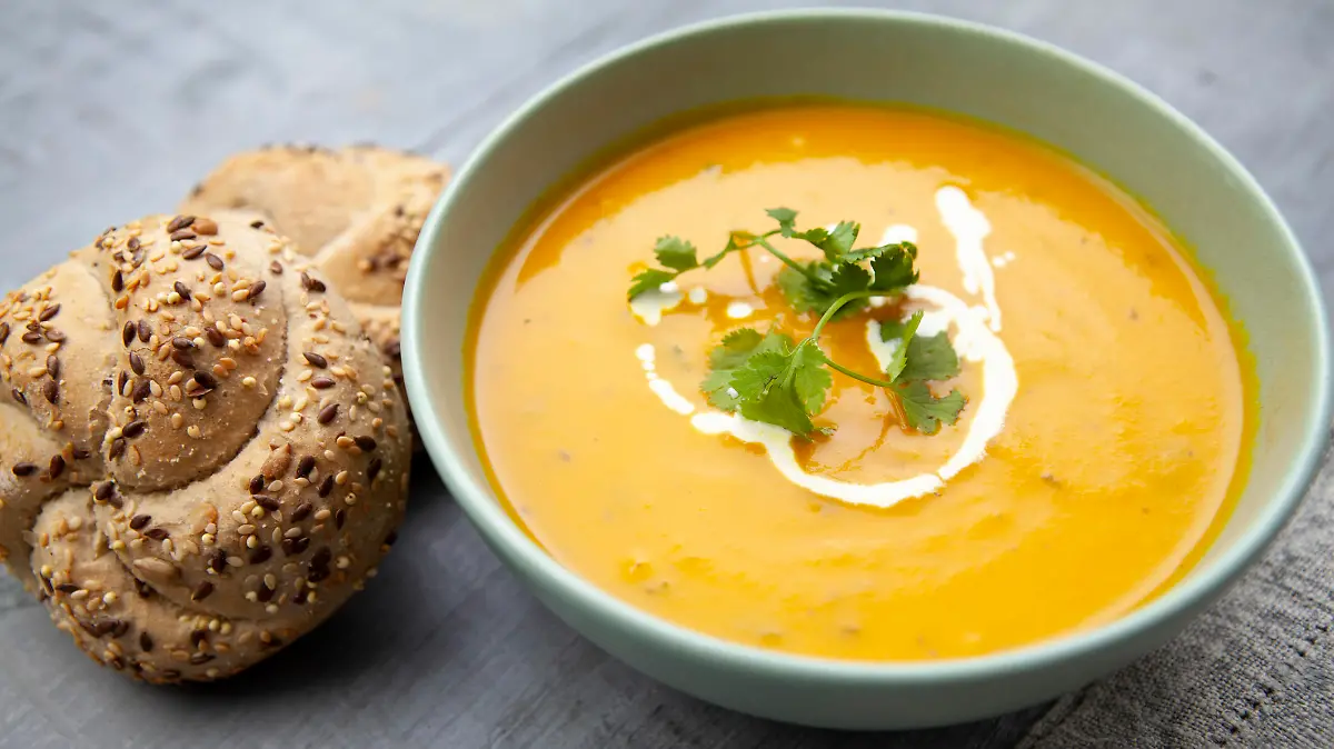 Healthy meal of carrot and coriander soup with bread rolls - photographed in a rustic setting
