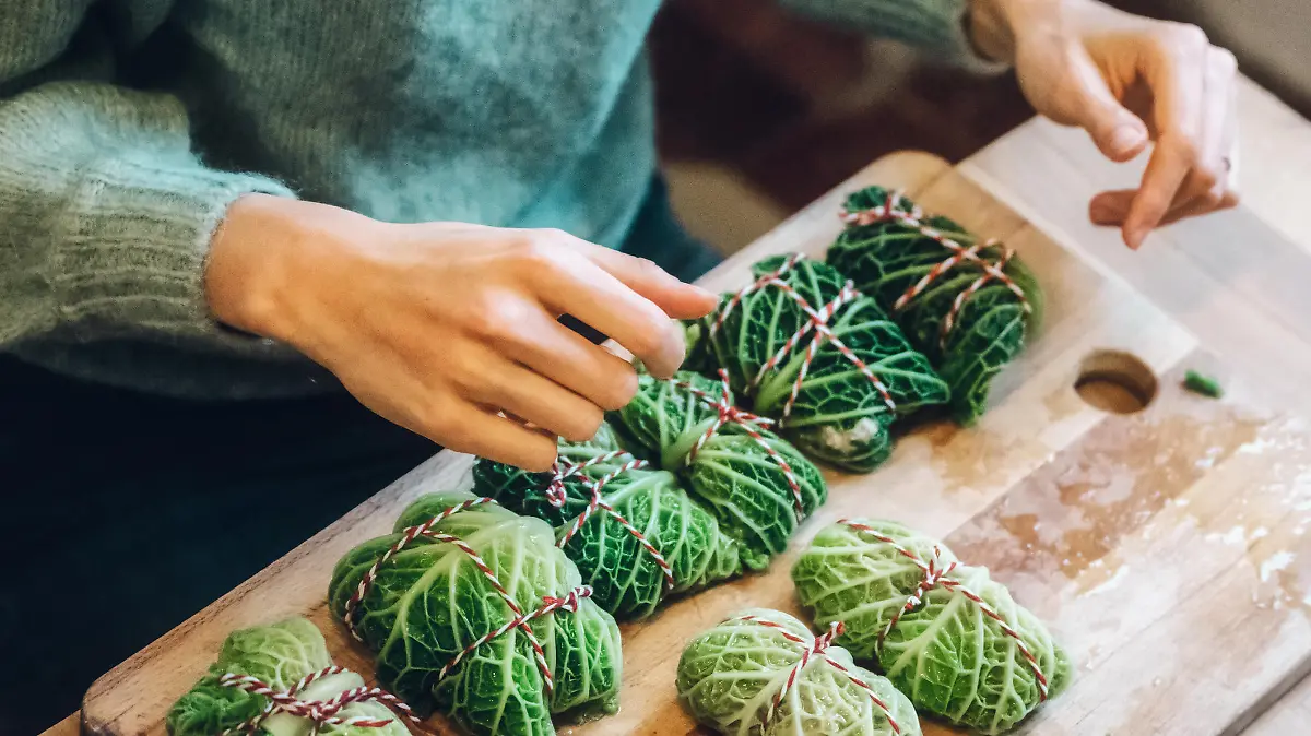high angle  view on female hands preparing savoy cabbage rolls on wooden kitchen board