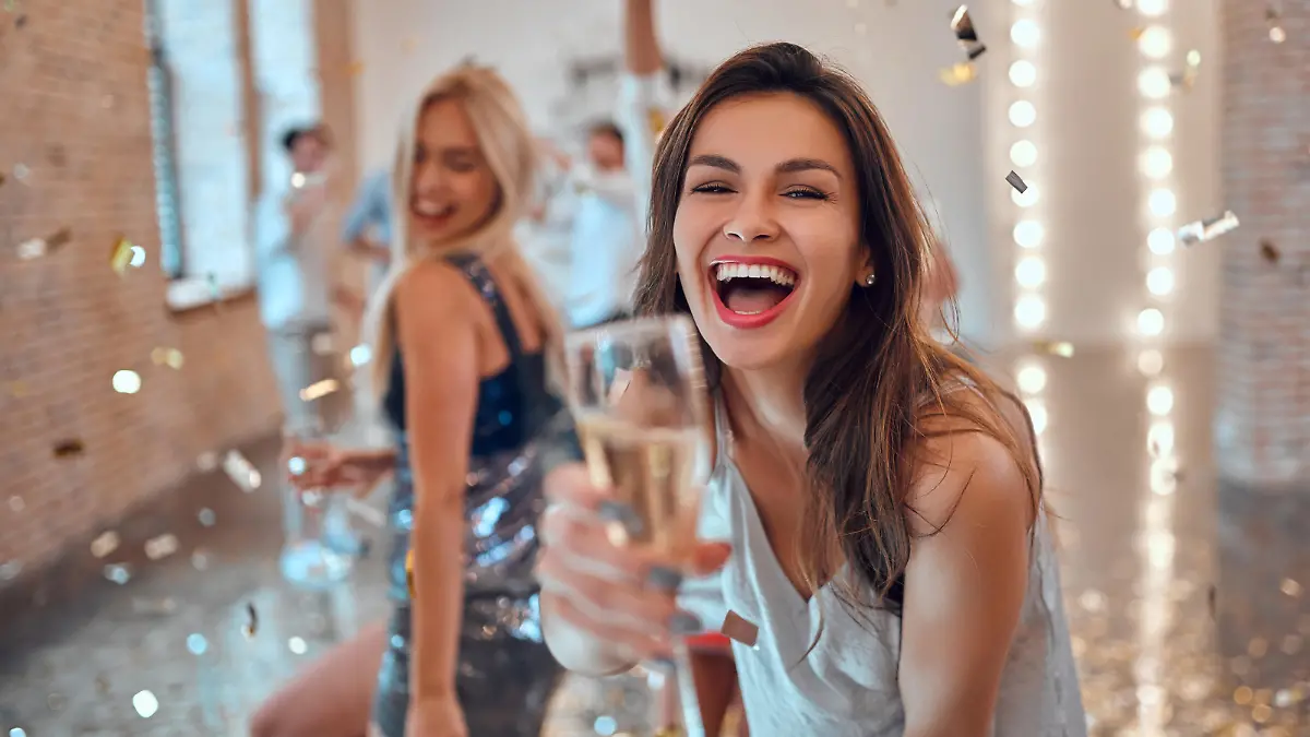 Let the party begin! Group of young people having fun together. Dancing in big light room with champagne and confetti falling. Celebrating holiday in big company of close friends.