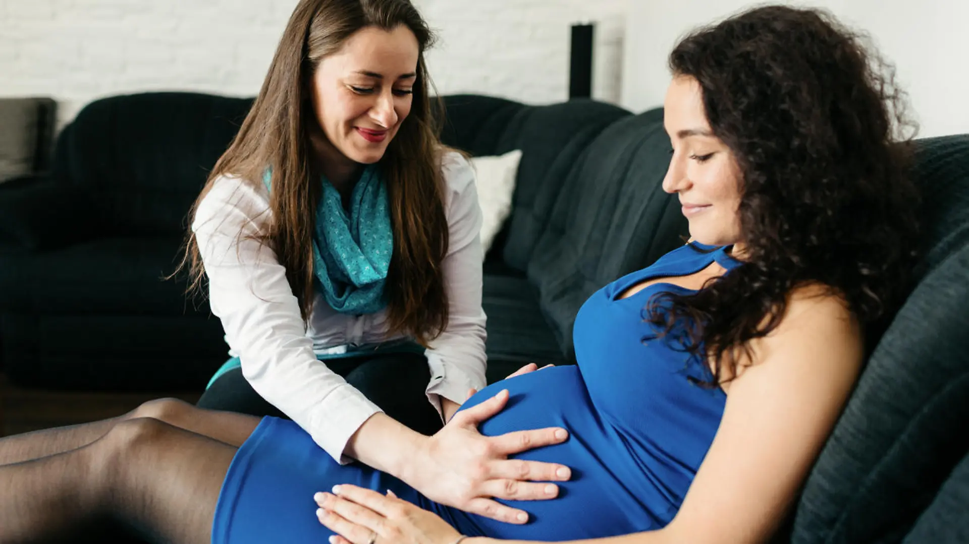 Doula fasst schwangerer Frau an den Bauch