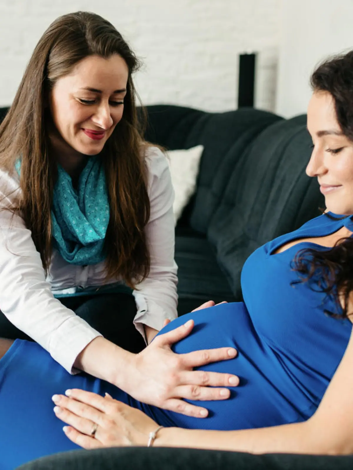 Doula fasst schwangerer Frau an den Bauch