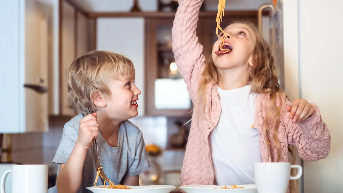 Cute children having fun while eating spaghetti with bolognese sauce at home