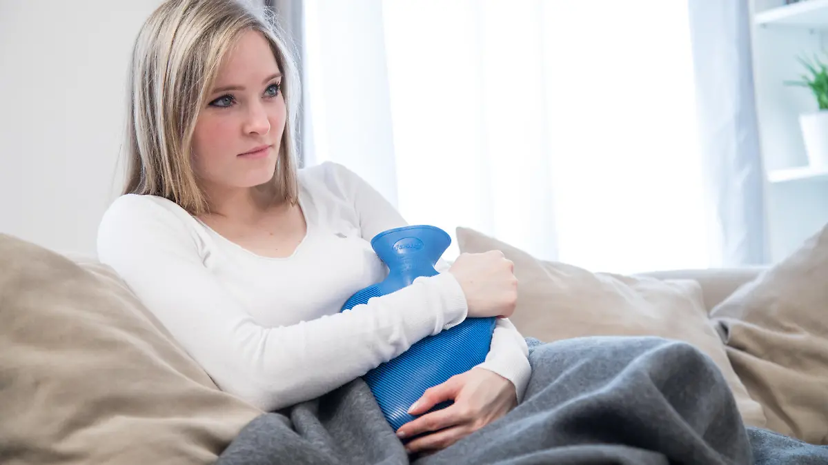 ILLUSTRATION - Eine junge Frau sitzt am 22.03.2017 in einem Wohnzimmer in Hamburg und haelt eine Waermflasche an den Bauch (gestellte Szene). Foto: Christin Klose || Modellfreigabe vorhanden
