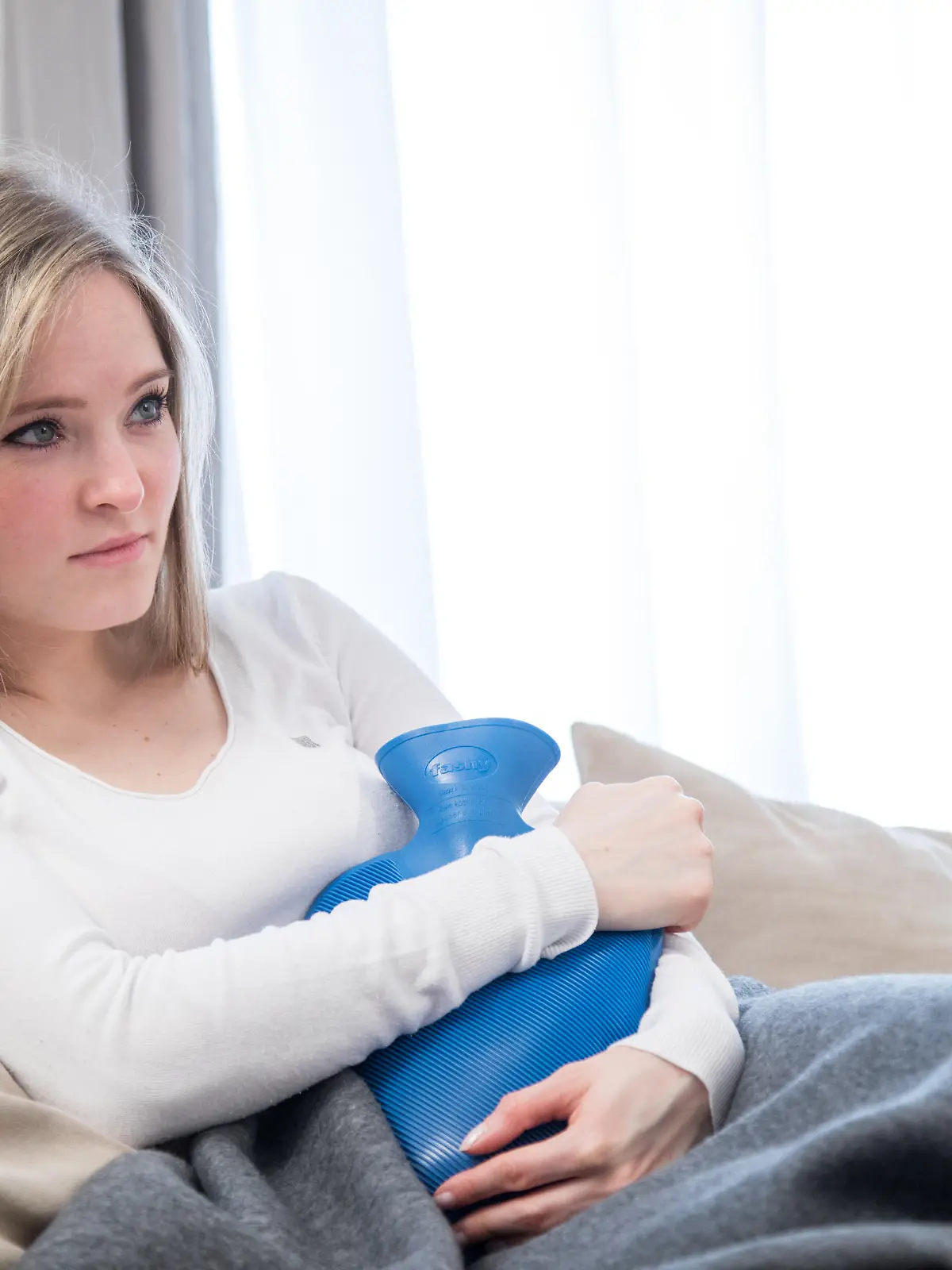 ILLUSTRATION - Eine junge Frau sitzt am 22.03.2017 in einem Wohnzimmer in Hamburg und haelt eine Waermflasche an den Bauch (gestellte Szene). Foto: Christin Klose || Modellfreigabe vorhanden