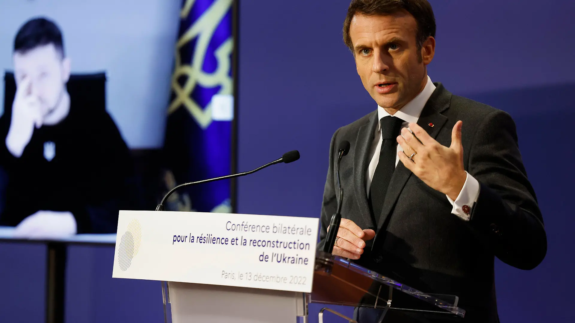 13.12.2022, Frankreich, Paris: Emmanuel Macron (r), Präsident von Frankreich hält eine Rede, während Wolodymyr Selenskyj, Präsident der Ukraine, über eine Videoverbindung an der französisch-ukrainischen Konferenz für Resilienz und Wiederaufbau teilnimmt. Foto: Ludovic Marin/POOL AFP/AP/dpa +++ dpa-Bildfunk +++