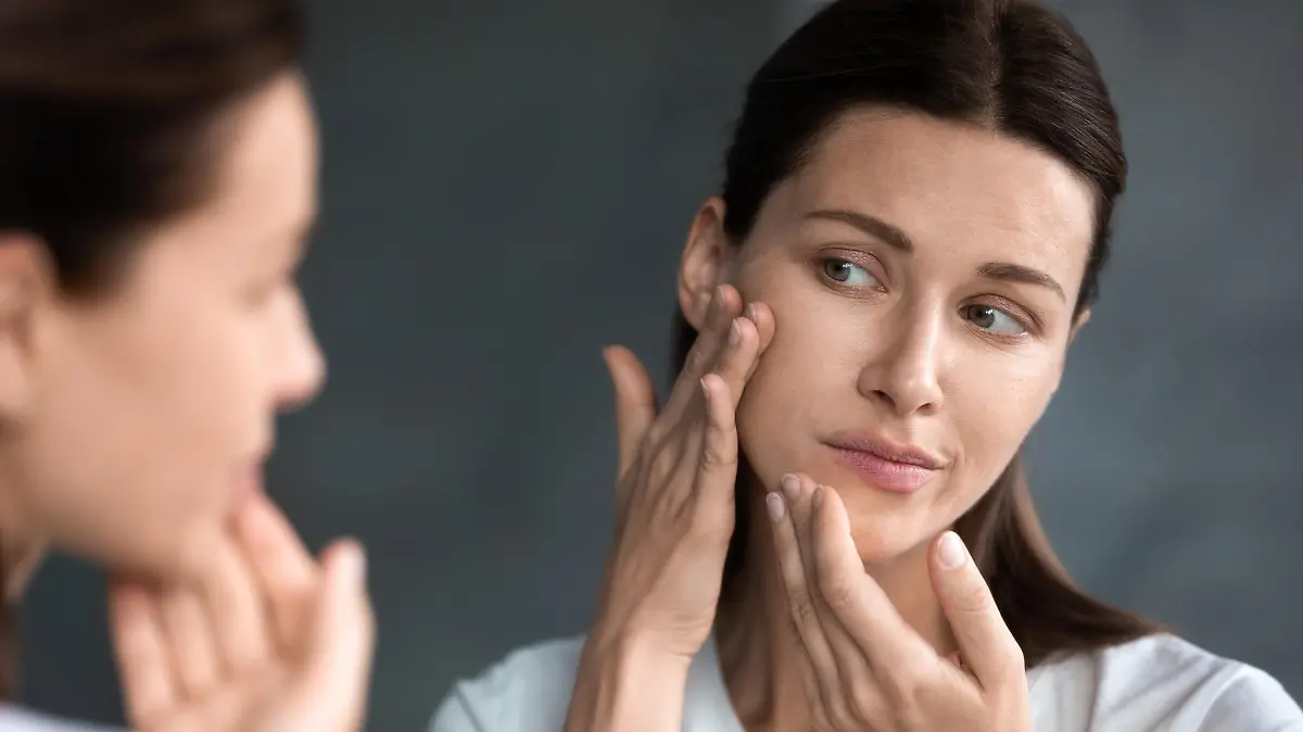 Close up unhappy sad woman looking at red acne spots on chin in mirror, upset young female dissatisfied by unhealthy skin, touching, checking dry irritated face skin, skincare and treatment concept