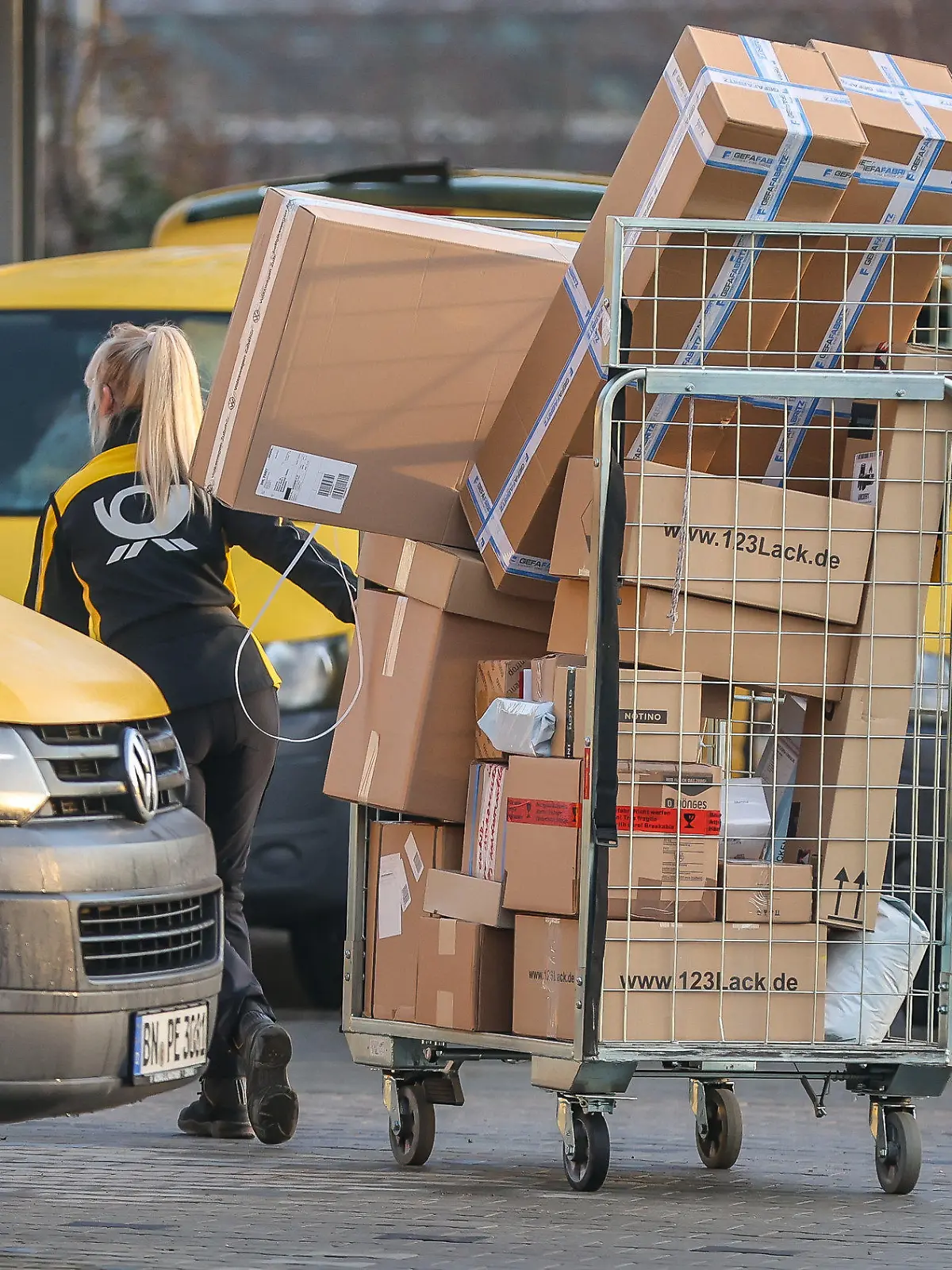 25.11.2022, Sachsen-Anhalt, Bitterfeld-Wolfen: Eine Mitarbeiterin der Deutsche Post DHL zieht einen vollen Paketwagen zu ihren Fahrzeug über den Hof eines Zustellpunktes. Die Wochen vor Weihnachten bedeutet traditionell Hochbetrieb bei den Logistikunternehmen. Tage mit Rabattaktionen wie dem Black Friday steigern das Paketaufkommen zusätzlich. Foto: Jan Woitas/dpa +++ dpa-Bildfunk +++