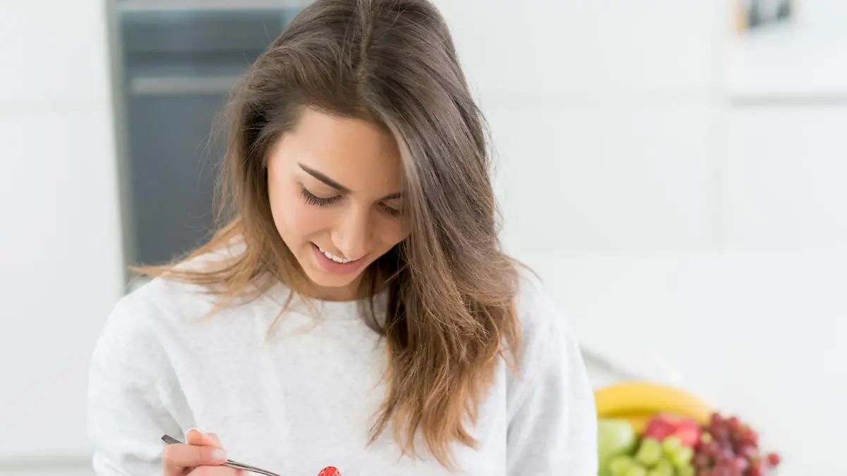 Beautiful young woman eating a healthy breakfast at home and smiling