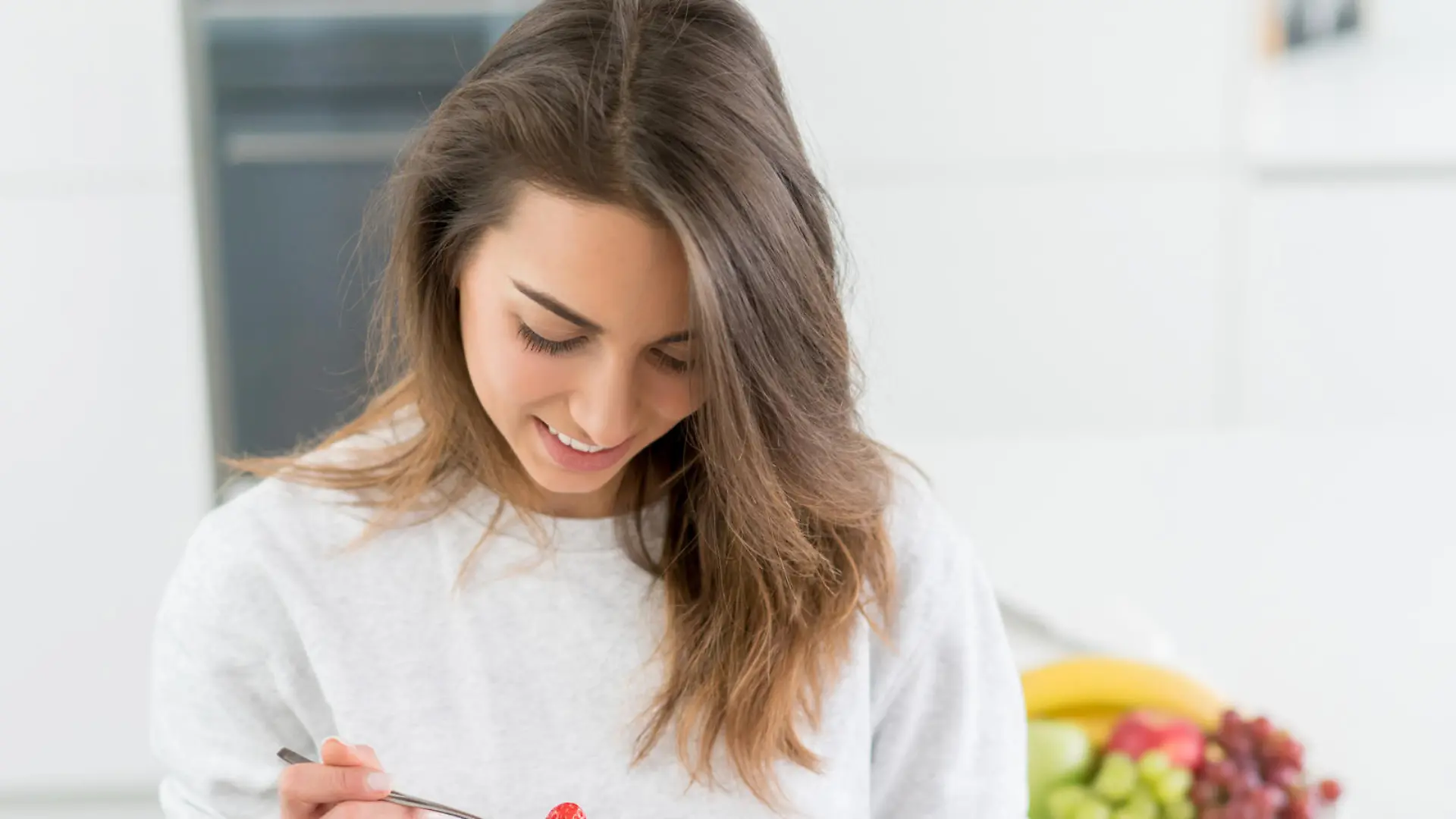 Beautiful young woman eating a healthy breakfast at home and smiling