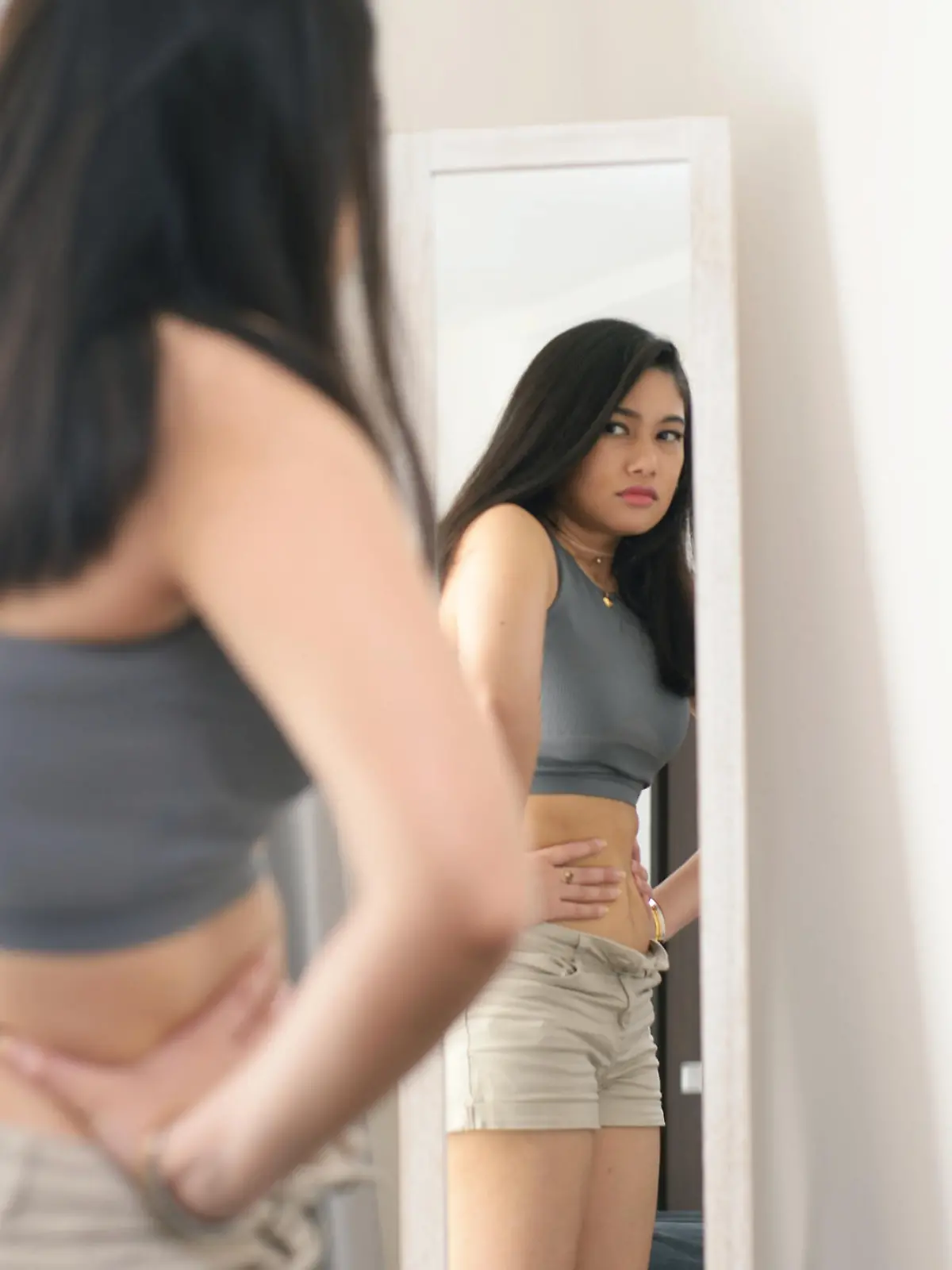 A young woman looking at her reflection in the mirror, unhappy with what she is seeing.