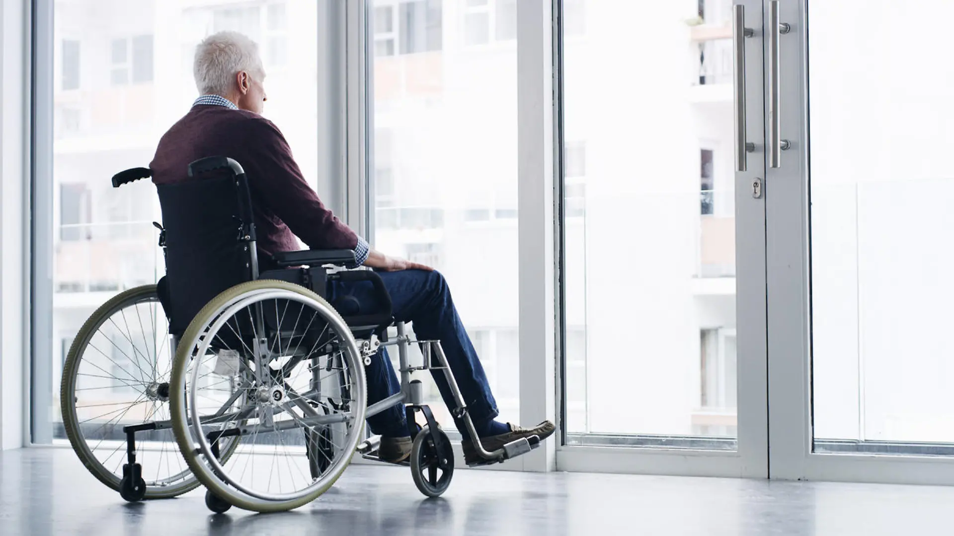 Shot of a senior woman in a wheelchair looking thoughtfully out of a window at home
