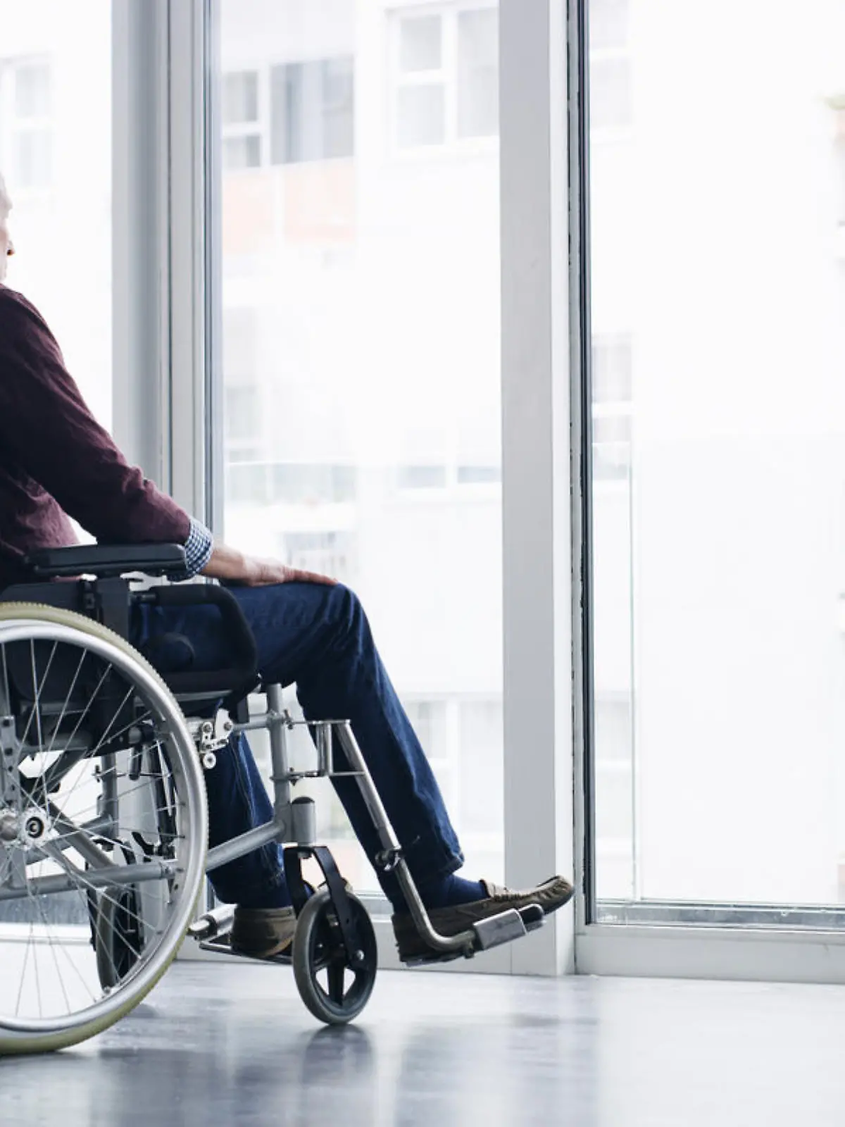 Shot of a senior woman in a wheelchair looking thoughtfully out of a window at home