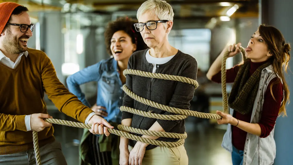 Team of happy creative people tying up an old-fashioned businesswoman in the office.