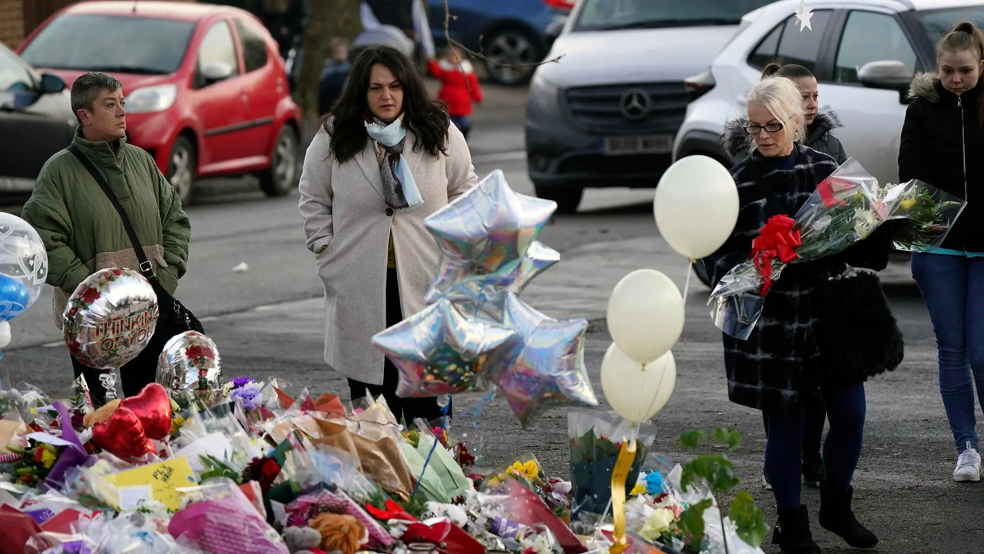 People look at flowers and tributes near to Babbs Mill Park in Kingshurst, Solihull, Tuesday Dec. 13, 2022 after the deaths of three boys aged eight, 10 and 11 who fell through ice into a lake in the West Midlands. (Jacob King/PA via AP)