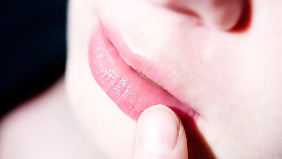 ILLUSTRATION - Eine Frau befühlt mit einem Finger eine juckende und schmerzende Stelle auf ihrer Lippe. Foto: Franziska Gabbert