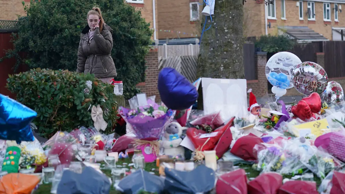A woman lays flowers among the tributes near to Babbs Mill Park in Kingshurst, Solihull, Tuesday Dec. 13, 2022 after the deaths of three boys aged eight, 10 and 11 who fell through ice into a lake in the West Midlands. (Jacob King/PA via AP)