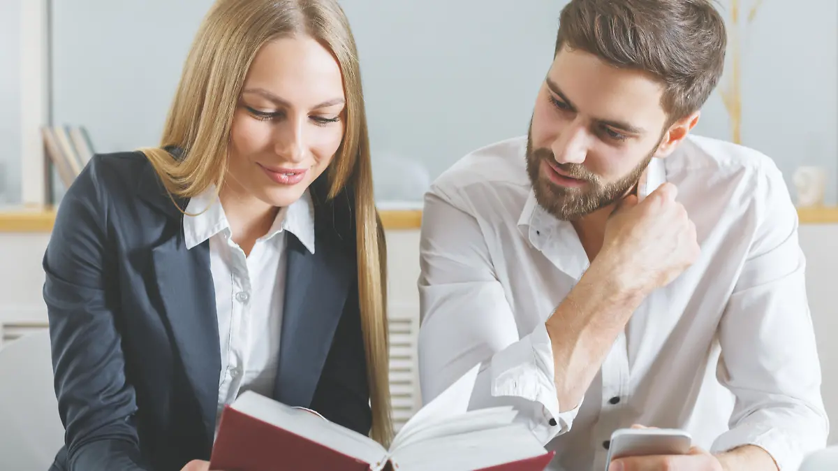 Attractive young man and woman reading book together at workplace. Knowledge concept