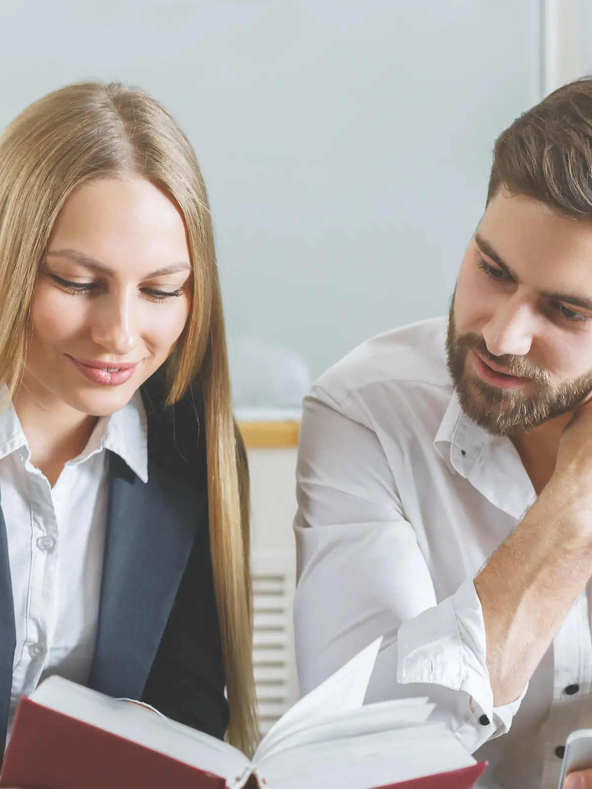 Attractive young man and woman reading book together at workplace. Knowledge concept
