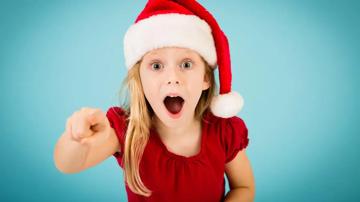 Color image of a surprised, blond-haired little girl wearing a Santa hat and pointing her finger. 