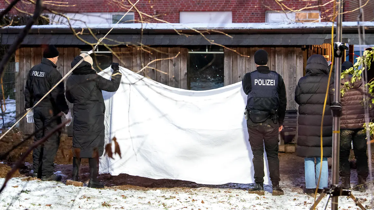 12.12.2022, Schleswig-Holstein, Alt Mölln: Ermittler der Polizei stehen hinter einem Mehrfamilienhaus in einem Garten an einem Erdloch und halten einen Sichtschutz hoch. Dort wurde am Mittag eine vergrabene Leiche gefunden. Foto: Daniel Bockwoldt/dpa +++ dpa-Bildfunk +++