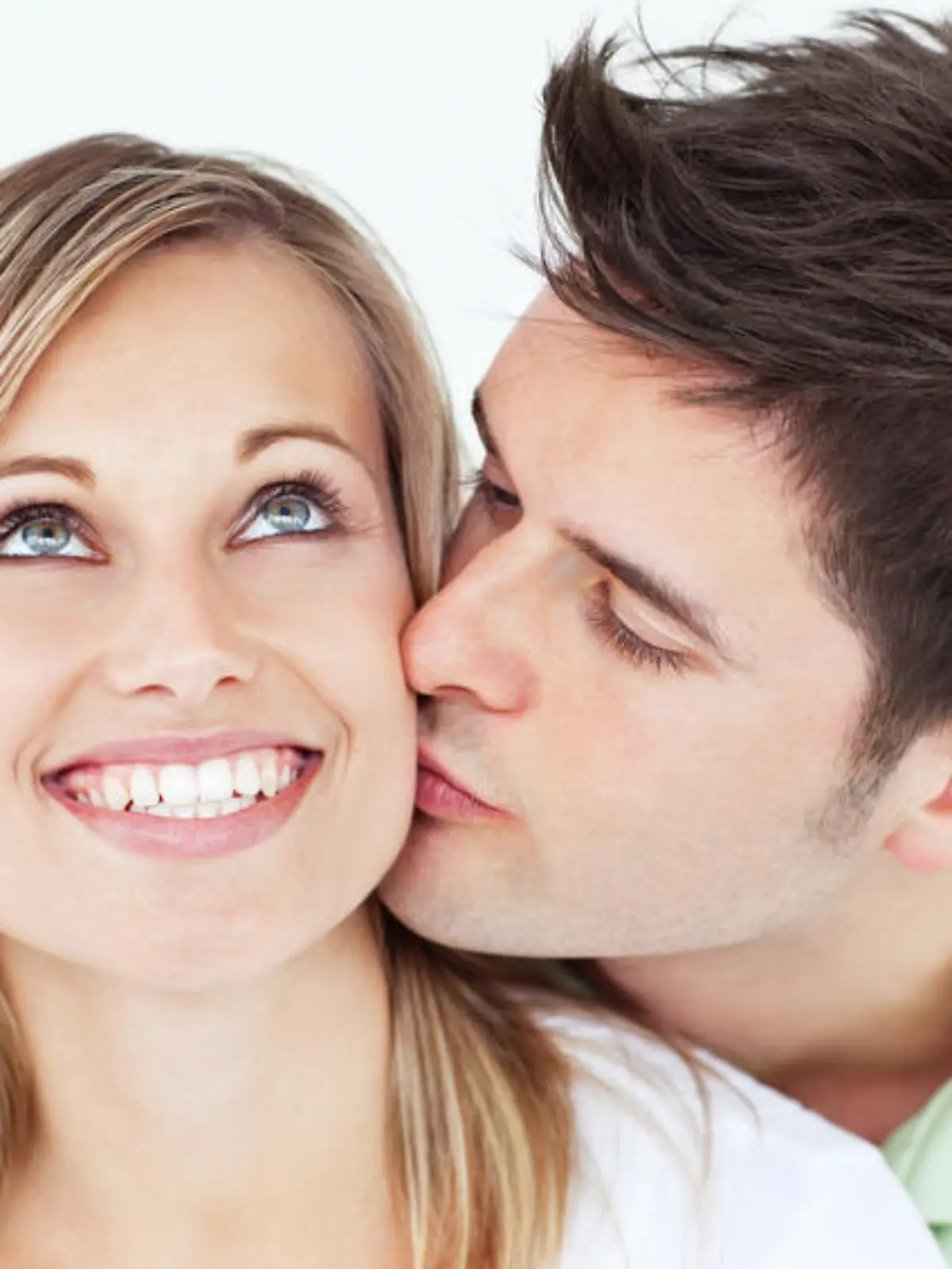 careful man kissing his smiling girlfriend against a white background